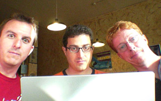 A picture of Doug, Tantek, and Eric peering over the display panel of Tantek's TiBook.