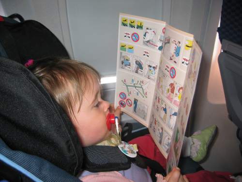 Safety first! Carolyn, strapped into her seat on the plane, solemnly looks over the airline safety information card.
